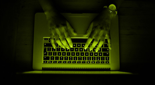 zwei Hände tippen auf einer grünlich leuchtenden Tastatur