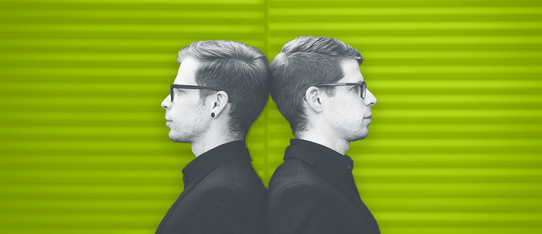 Zwei Männer stehen Rücken an Rücken vor einer grünen Wand