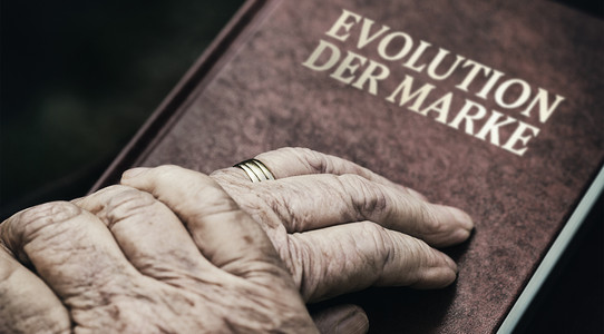 ein Paar Hände einer älteren Person liegen auf einem Buch mit dem Titel "Evolution der Marke"