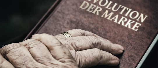 ein Paar Hände einer älteren Person liegen auf einem Buch mit dem Titel "Evolution der Marke"