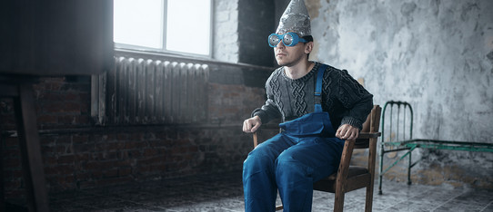 ein Mann mit Aluhut und Brille sitzt auf einem Holzstuhl